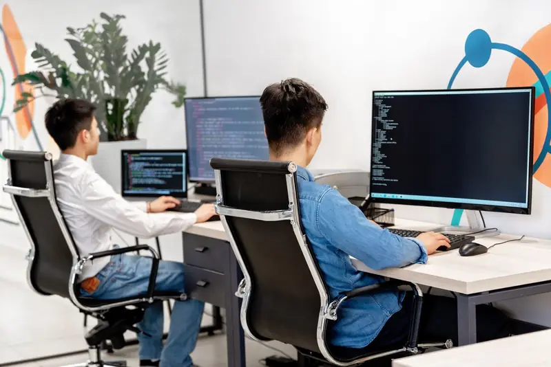 Dos desarrolladores trabajando en sus escritorios frente a monitores con código